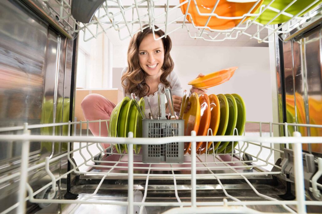 A woman smiles as she loads colorful plates into a dishwasher.