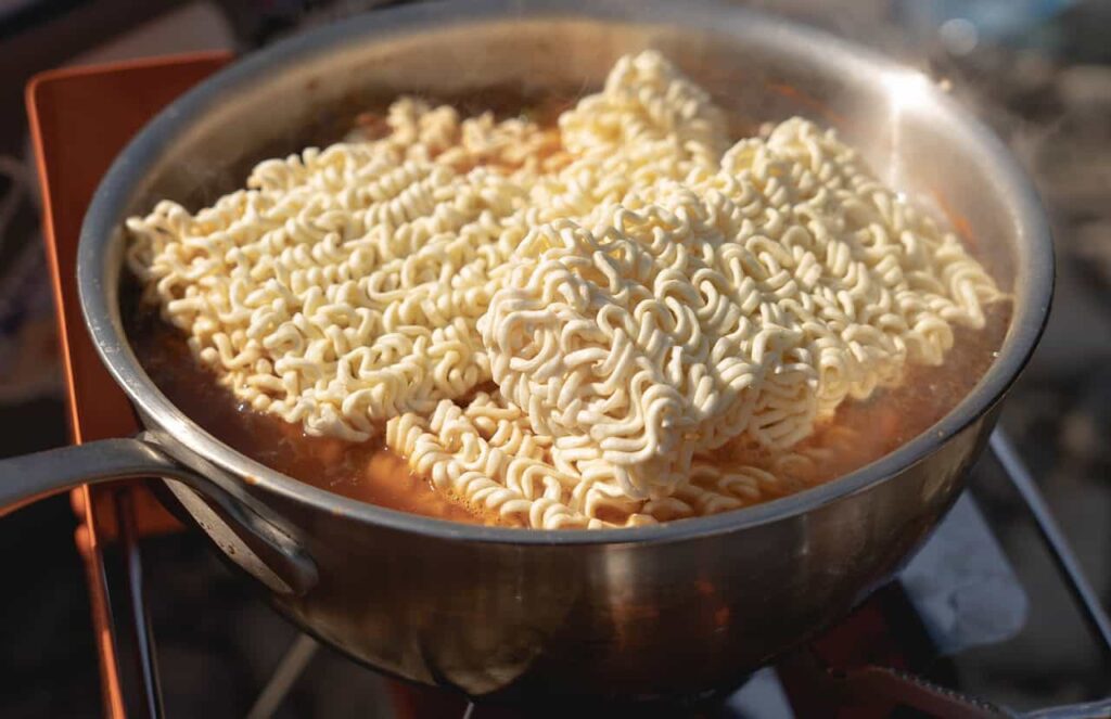 A pot of boiling water with uncooked instant ramen noodles being prepared on a stove.