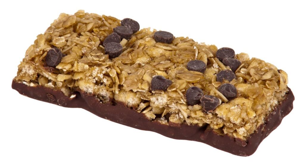 A granola bar topped with oats and chocolate chips, with a chocolate-coated bottom.