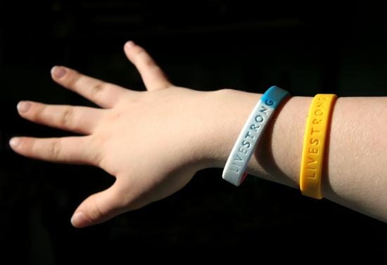 A hand wearing two LIVESTRONG wristbands, one yellow and one white with blue accents.