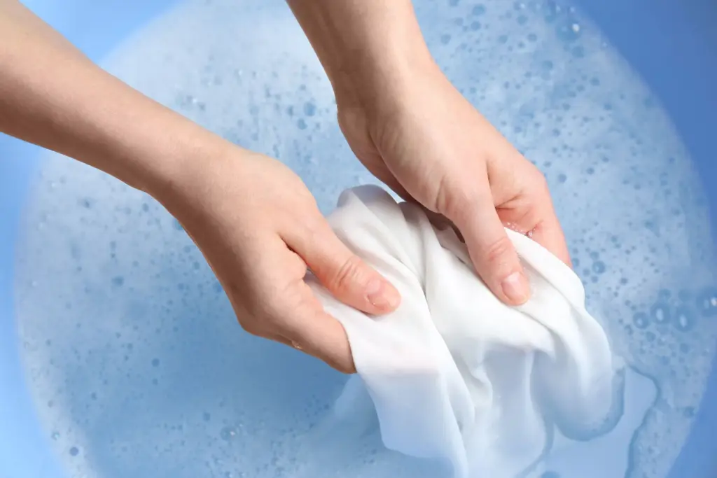 Hands washing a white cloth in soapy water in a blue basin.
