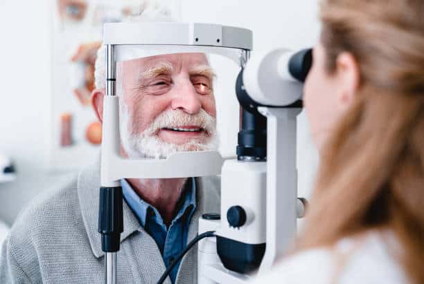 An elderly man undergoing an eye examination with an ophthalmologist using specialized medical equipment.