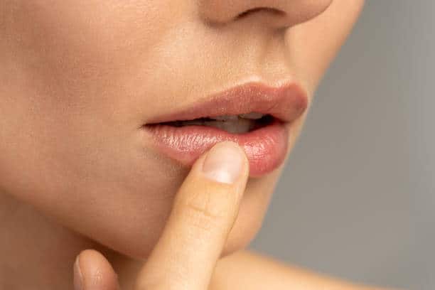 Close-up of a person's lips and finger, showing them touching their bottom lip gently. The background is blurred, focusing attention on the lips and finger.