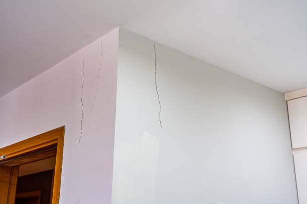 Interior wall with visible vertical cracks near the ceiling and doorway. The cracks run down the white wall from the ceiling edge.