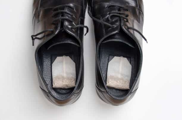 Two black dress shoes with tea bags placed inside each shoe on a white background.