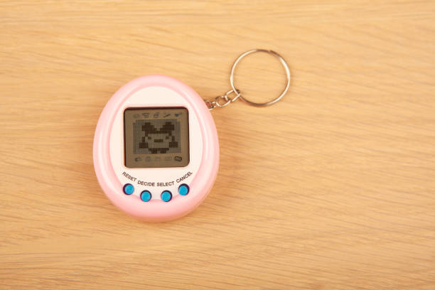 A pink, egg-shaped digital pet toy with a keychain and three blue buttons, displayed on a wooden surface.