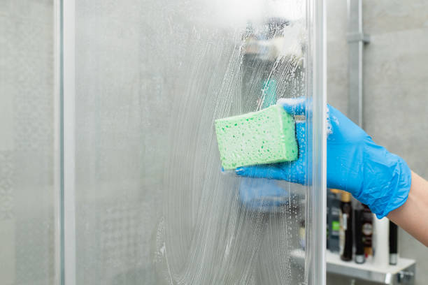 A hand in a blue glove is cleaning a glass surface with a green sponge.