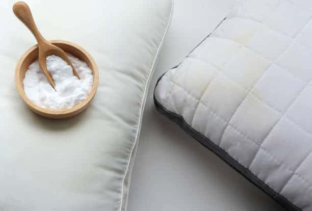 Two pillows are shown, one quilted and the other smooth. A wooden bowl with a wooden spoon containing white powder is placed on the smoother pillow.