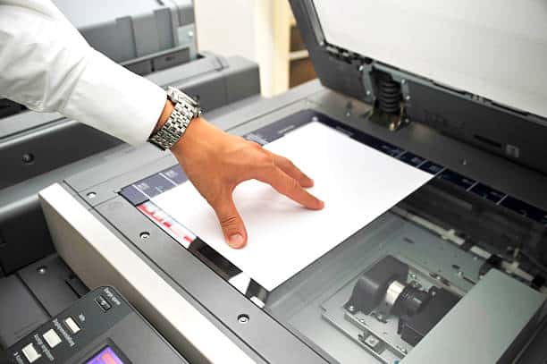 A person places a sheet of paper on a photocopier's glass scanning surface, preparing to make a copy.