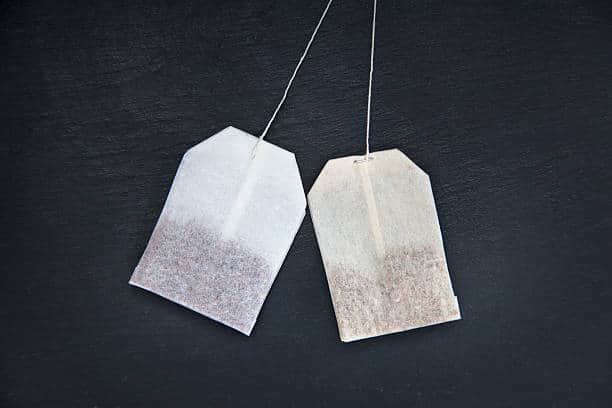Two tea bags with strings attached are placed side by side on a dark surface.