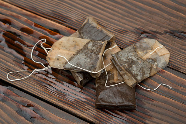 A few used tea bags are laid out on a wet wooden surface.