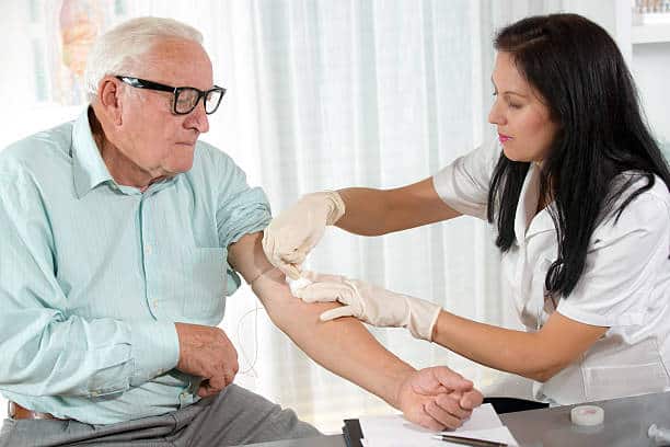 A healthcare professional administers a vaccination to an elderly man seated in a clinical setting.