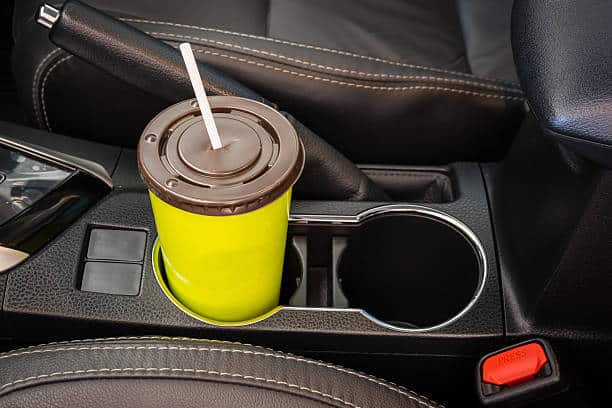 A yellow cup with a straw in the car's cup holder next to the gear shift lever.