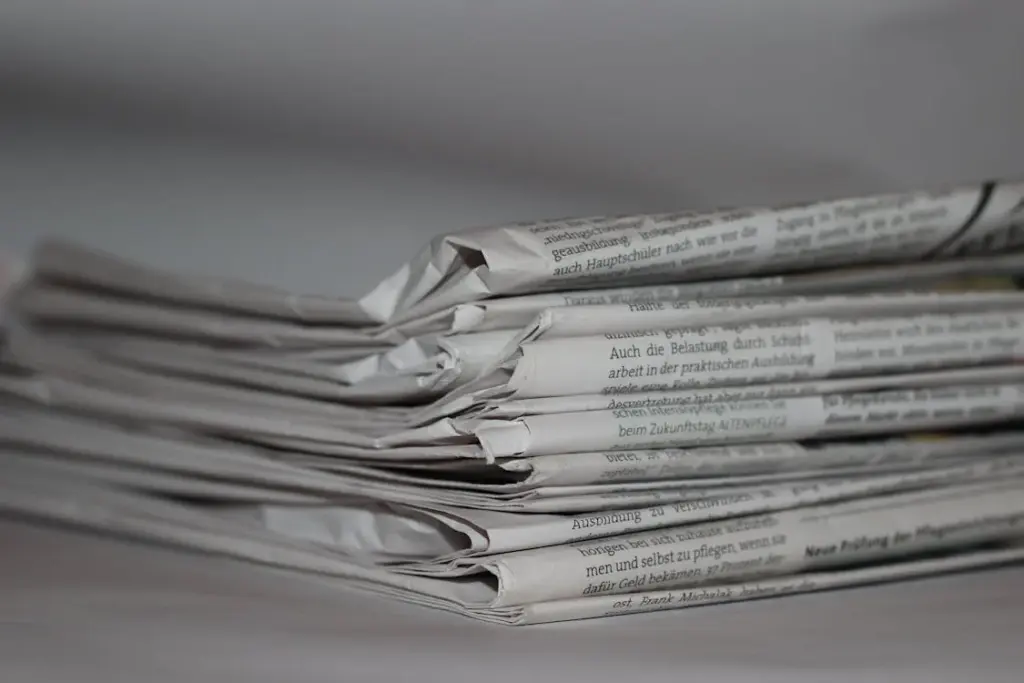A close-up of a stack of folded newspapers on a white surface. Text is visible on the pages, but is not legible.
