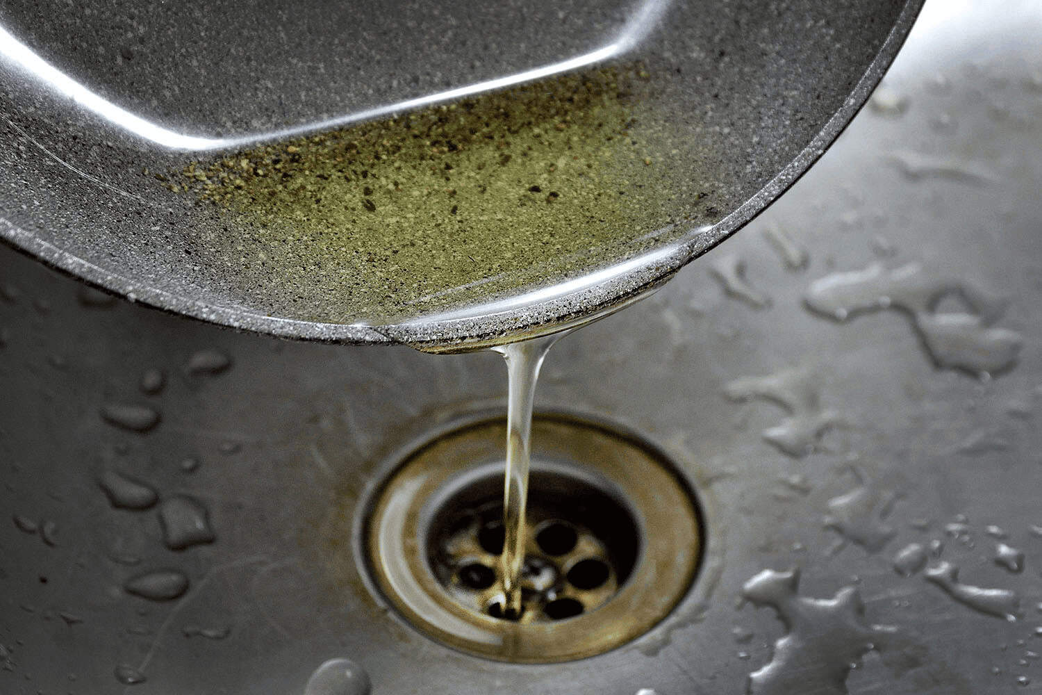 Cooking oil being poured down a kitchen sink drain.