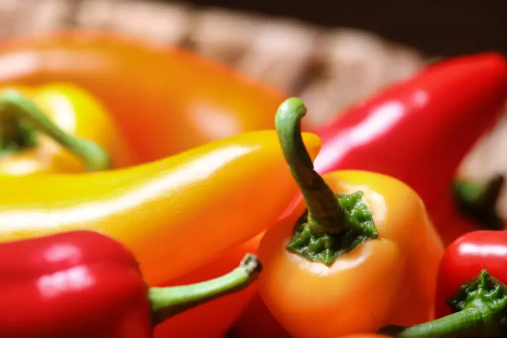 Close-up of a variety of fresh yellow and red bell peppers with stems, arranged together.