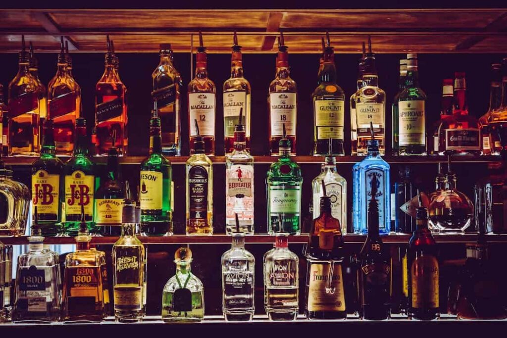 A variety of liquor bottles are displayed on illuminated shelves, including whiskey, rum, gin, and vodka.