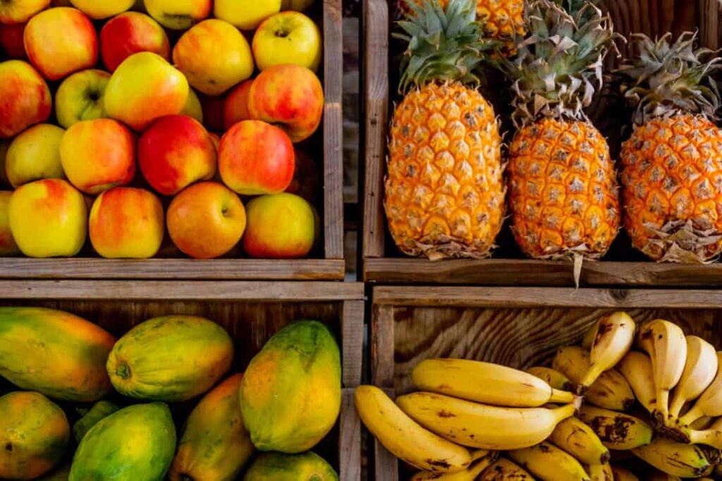 A wooden crate filled with apples, another with pineapples, a third with papayas, and a fourth with bananas.