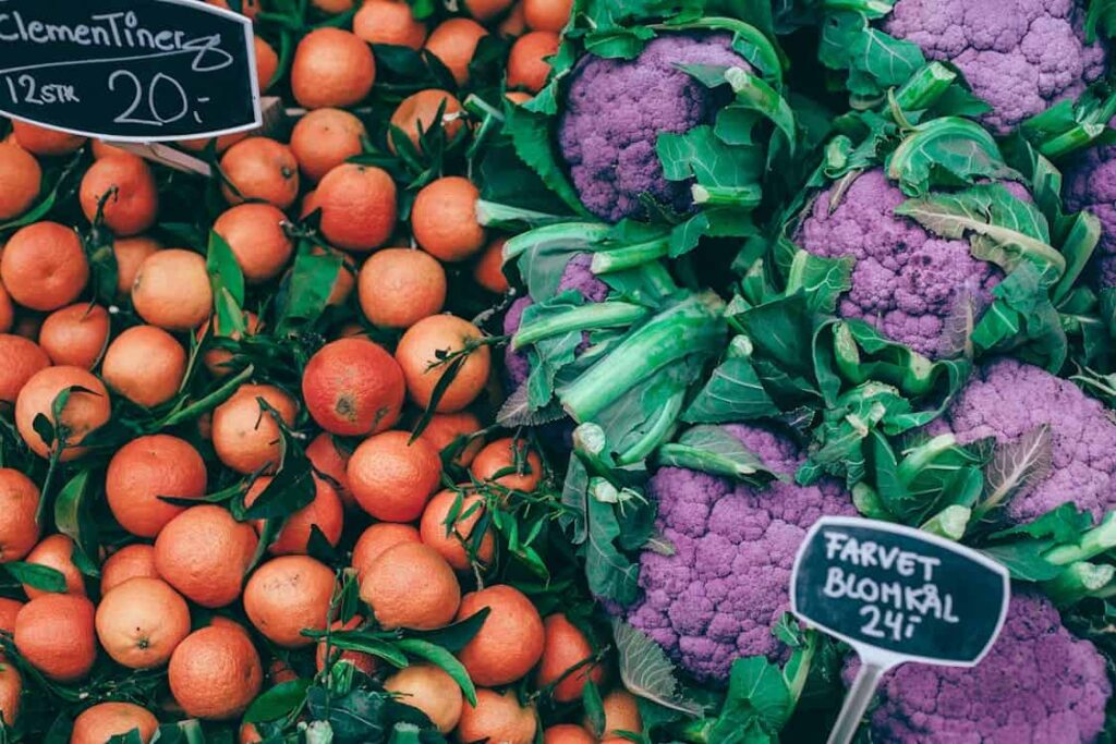 A market display with clementines on the left, priced at 20 per dozen, and purple cauliflower on the right, priced at 24 each.