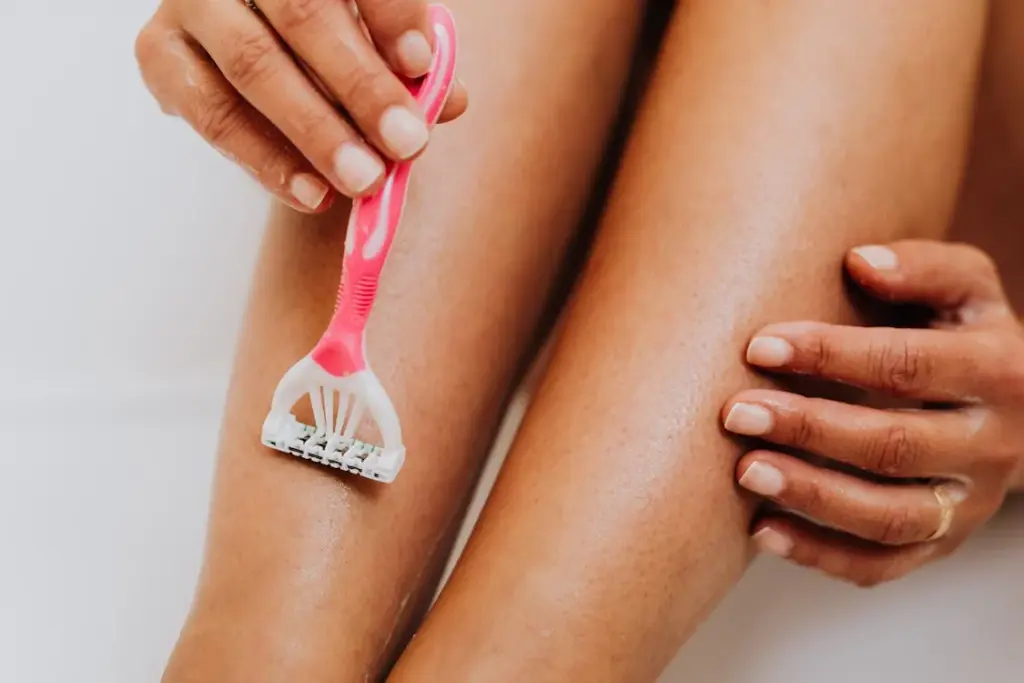Person using a pink razor to shave their leg.