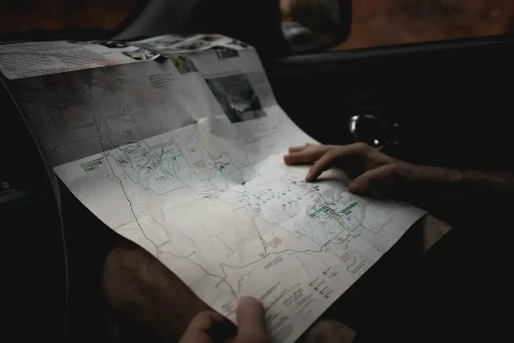 A person holding a detailed map while sitting inside a vehicle, closely examining the terrain and route information.