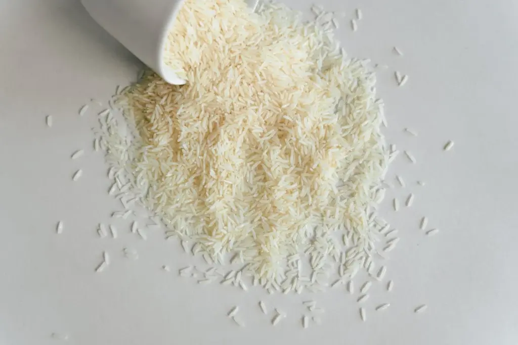 Uncooked white rice spilling out from a white container onto a light surface.