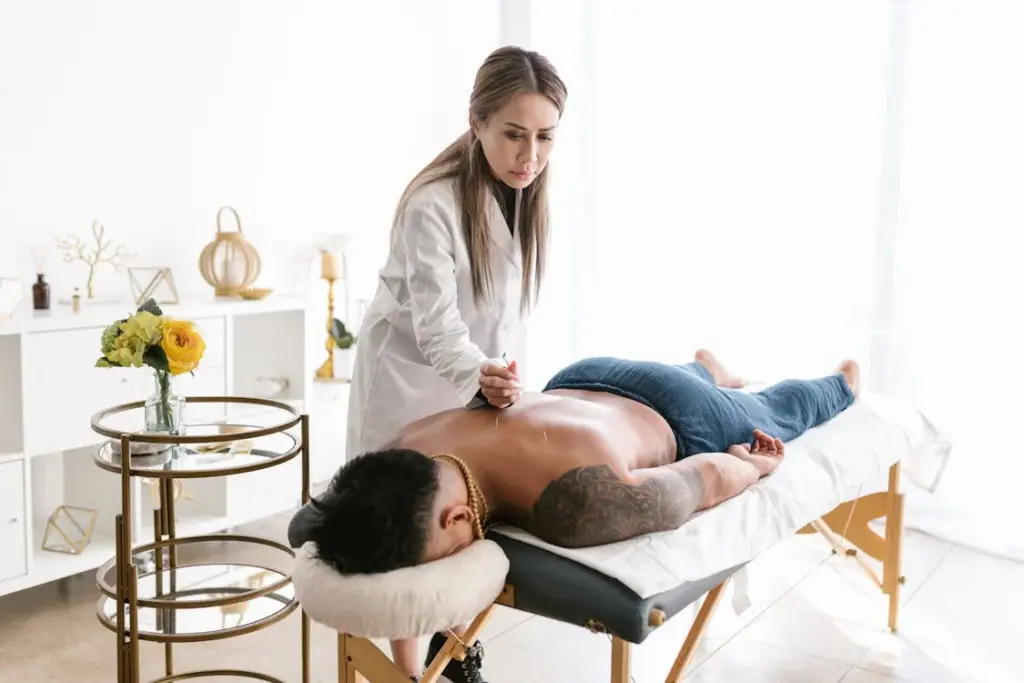 A massage therapist presses her hands on a client's back during a treatment session in a bright room with a white decor.