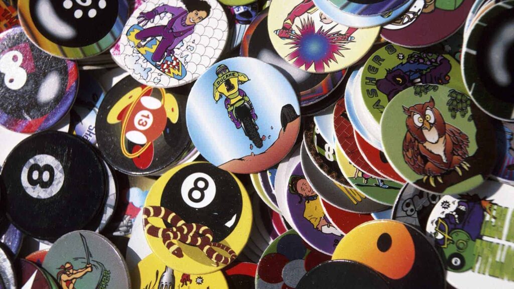 A scattered assortment of colorful Pogs featuring various designs including sports, animals, and cartoon characters.
