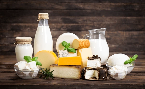 A variety of dairy products, including milk, cheese, cream cheese, and yogurt, arranged on a wooden surface with garnishes.