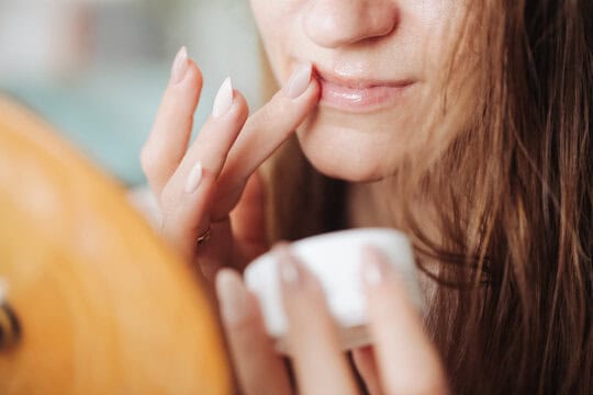 Close-up of a person applying lip balm with a finger, holding a small container.