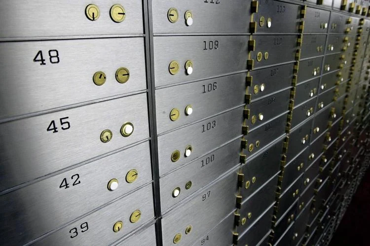 Rows of gray metallic safe deposit boxes with yellow keyholes in a secure storage facility. Each box is numbered.
