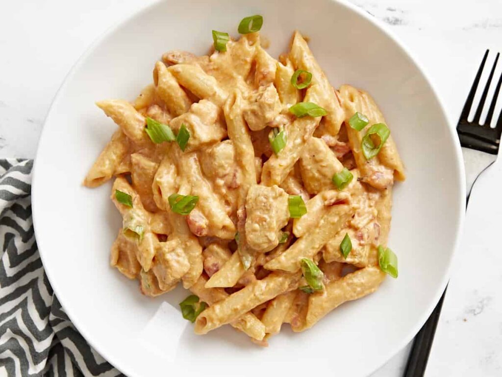 A bowl of creamy penne pasta with sliced green onions on top.