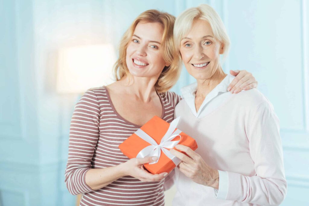 Two women smiling and holding an orange gift box with a white ribbon.