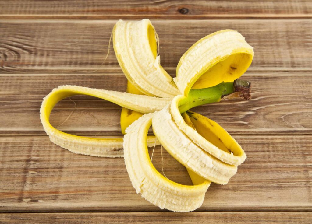 A partially peeled banana rests on a wooden surface, showing its yellow skin and inner fruit.