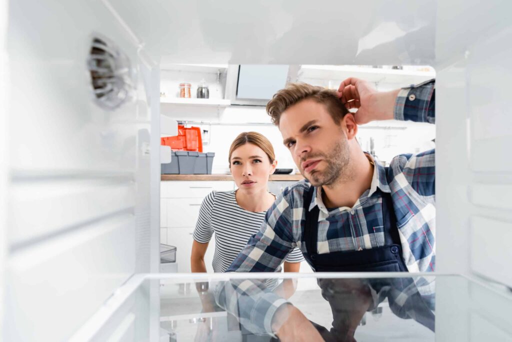 A man and woman look confusedly into an empty refrigerator.