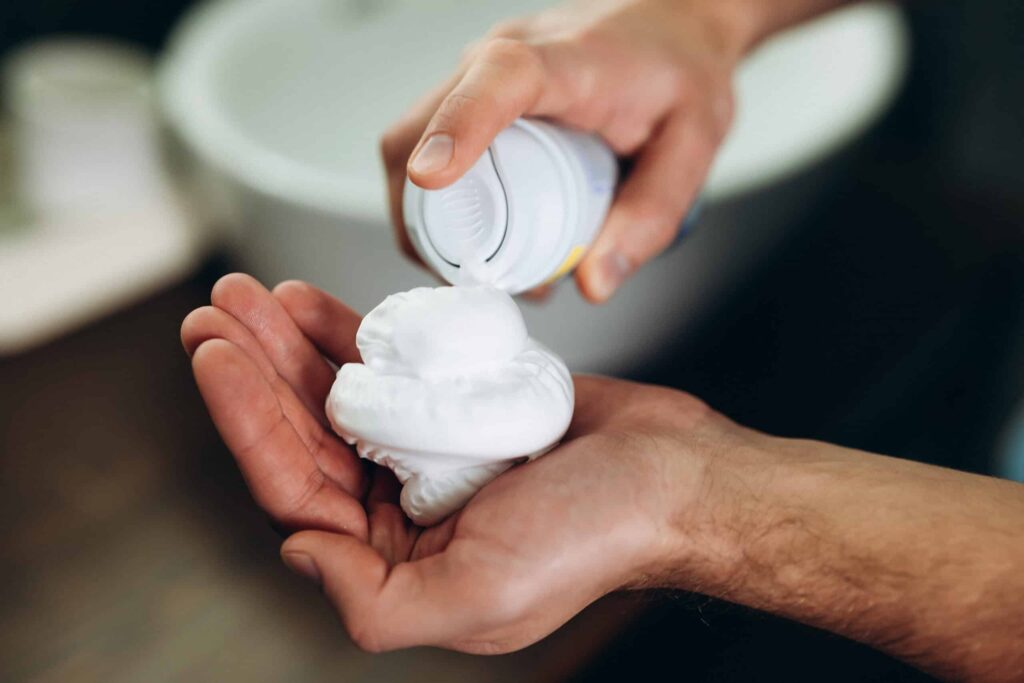 A person dispensing shaving cream from a can into their hand.