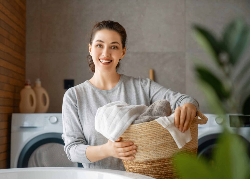 A person in a laundry room holds a basket of towels in front of a washing machine and dryer.