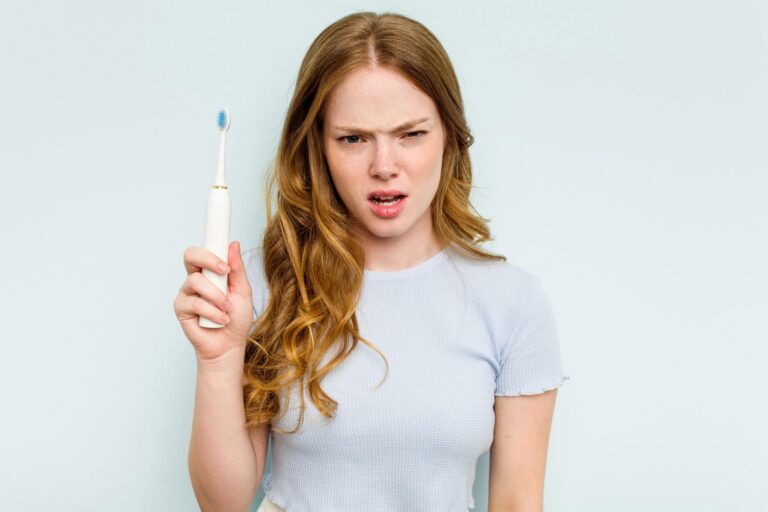 Person with long hair holding an electric toothbrush, looking puzzled.