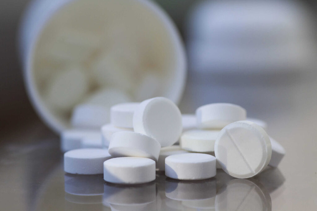 White round tablets scattered from an open bottle on a reflective surface.