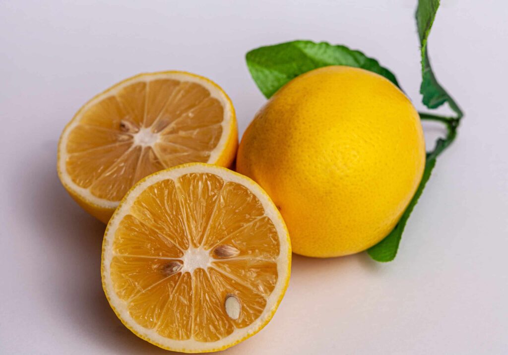 A whole lemon and two lemon halves are displayed against a plain background. A green leaf is attached to the whole lemon.
