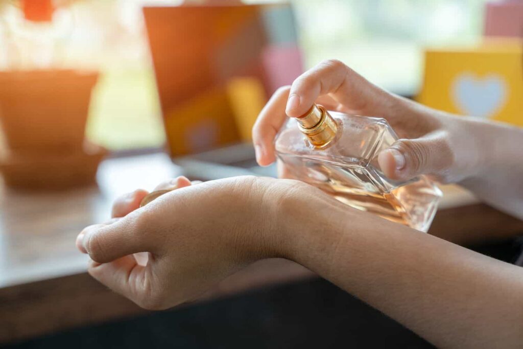 Hands applying perfume on the wrist from a spray bottle, with blurred background elements.