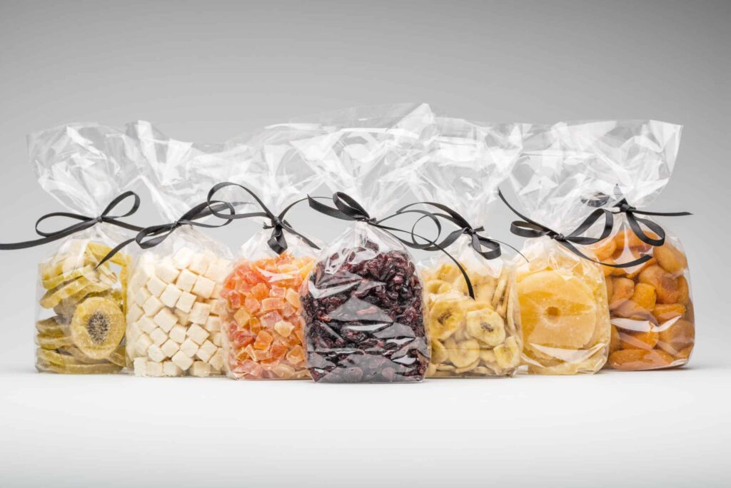 Bags of assorted dried fruits tied with black ribbons on a gray background.