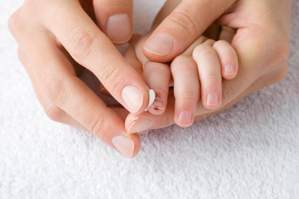 An adult's hands trim a baby's fingernails on a white towel.