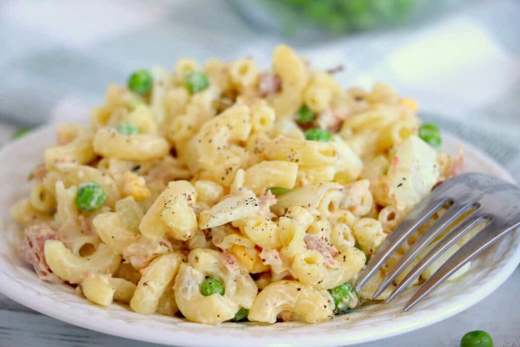 A plate of macaroni salad with peas and a fork on the side.