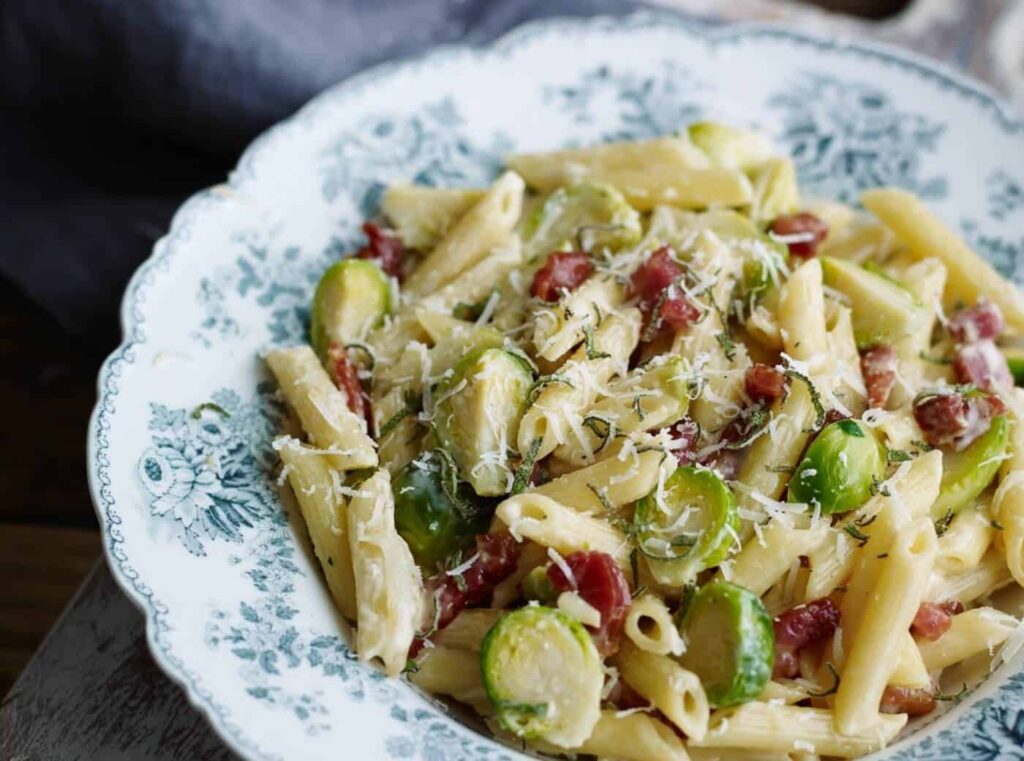 A plate of creamy penne pasta with Brussels sprouts, bacon, and grated cheese.