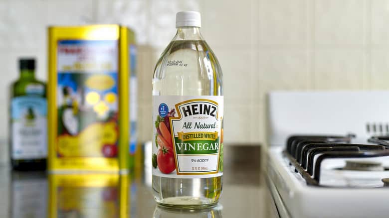 A bottle of Heinz distilled white vinegar is placed on a kitchen counter near a stove, with some other cooking items in the background.