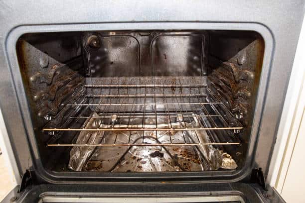 A dirty oven with two wire racks and visible grime on the interior surfaces. The bottom of the oven has burnt residue and aluminum foil covering part of the surface.