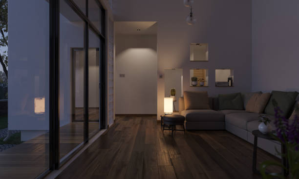 A modern living room with wooden flooring, large glass doors, a corner sofa, and a small illuminated lamp on a table.