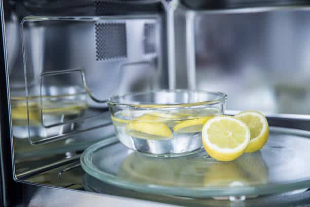 Glass bowl with lemon slices in water sits inside a microwave.