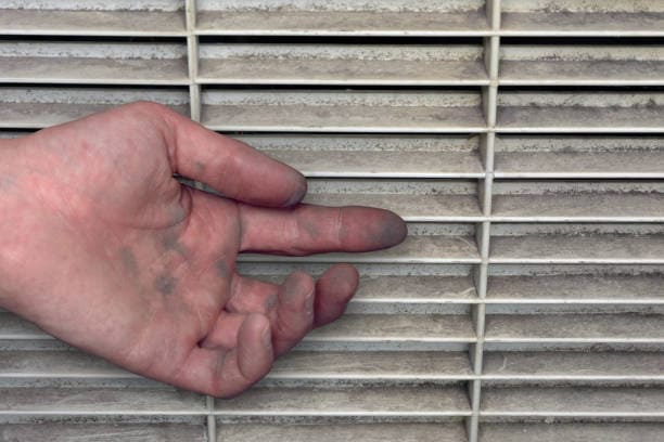 A hand with dirty fingers touches a dusty air vent.